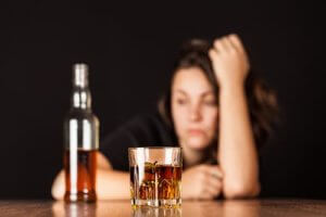 a woman sits in front of some liquor thinking about how she needs alcohol addiction rehab