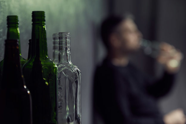 Man suffering from depression surrounded by alcohol bottles