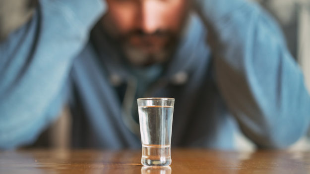 Man with alcohol addiction staring at a shot glass
